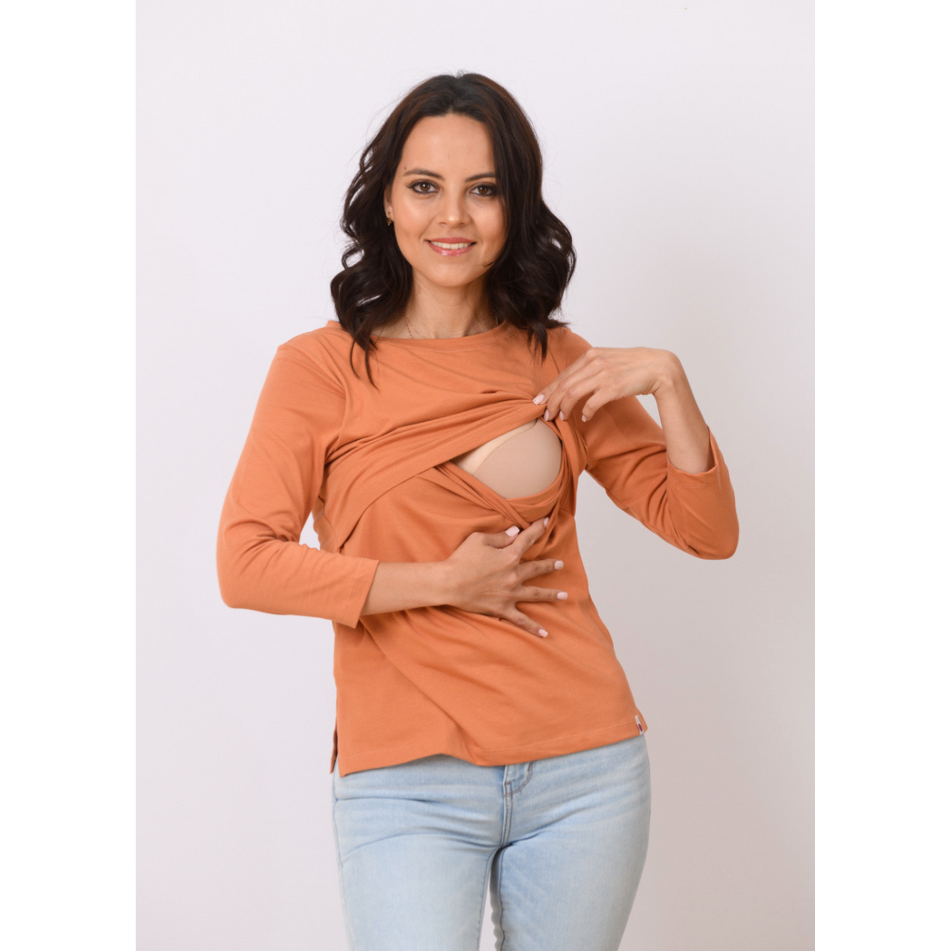 Woman demonstrating nursing access in rust orange nursing top with front-layered design for easy breastfeeding access.